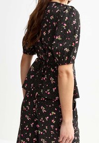 Top floral negro con mangas abullonadas, cintura ajustada y un diseño tipo peplum con patrones florales en rosa y blanco sobre un fondo de puntos.