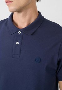 Marineblauwe polo shirt van textiel met structuur, voorzien van een drie-knopen sluiting en een klein geborduurd logo op de linkerkant van de borst.