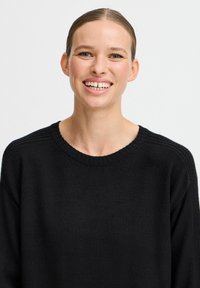 Maglione nero con scollo a girocollo a coste, tessuto testurizzato e design con spalle cadenti. Stile minimalista senza motivi o accenti evidenti.