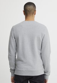 Sudadera gris de manga larga, con cuello redondo, puños y dobladillo acanalados, y una textura sutil. Presenta una pequeña etiqueta con el logo en el dobladillo inferior.