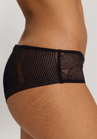 Mustat pitsiset hipster-alushousut, joissa on geometrija-kuvio ja läpinäkyviä osia. Reunat on viimeistelty pehmeällä mustalla trimmiä varten mukavuutta lisäämään.