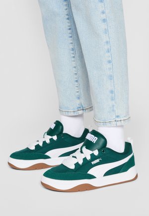 Zielone zamszowe i materiałowe sneakersy z białymi dodatkami, wyposażone w grube białe sznurowadła, wyściełany kołnierz i brązową gumową podeszwę.