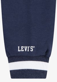 Sötétkék kötött pulóver anyag, fehér és szürke csíkos bordás mandzsettával. A mandzsettához közel elhelyezkedő fehér "LEVI'S®" logóval rendelkezik.