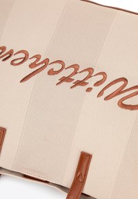 Sac fourre-tout en tissu beige avec des poignées en cuir marron, arborant un texte brodé marron. Le texte et le tissu présentent une finition texturée.