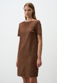 Bruine faux suede jurk met korte mouwen, een ronde halslijn en een rechte snit. Kenmerkt zich door een naad die verticaal over de voorkant loopt.
