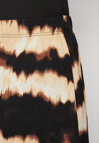 Sukňa s čierno-krémovým tie-dye vzorom s textúrovanou tkaninou, elastickým pásom a nerovnomernými vlnitými vzormi pozdĺž lemovania.