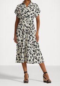 Květinové midi šaty v krémové barvě s černým listovým vzorem; krátké rukávy, stažený pas, vylepšeny černými sandály na platformě.