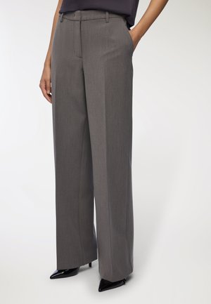 Pantaloni larghi grigi con una texture liscia, dotati di tasche frontali e una vestibilità su misura, abbinati a décolleté nere a punta.