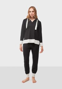 Sudadera negra con detalles en blanco, con cuello en V y lazo, combinada con pantalones deportivos negros a juego y puños acanalados blancos. Textura de tela suave.