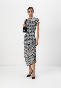 Black and white patterned dress, short sleeves, mid-length, with ruching detail at the side; paired with a black handbag and heels.