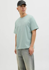 Lyseblå bomulds t-shirt med korte ærmer og rund halsudskæring, med hvid tekst der står "ORIGINALS" på fronten.