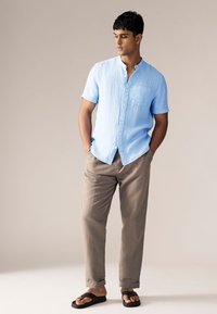 Hele sinine lühikeste varrukatega särk, millel on nööbitav eesmine osa ja tasku; kombineeritud beežide pükstega ja tumedate sandaalidega. Sile kangapind.