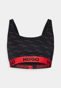 Melnā kroptopa krūšturis ar smalku pelēko "Hugo" teksta rakstu, kuram ir spilgti sarkans elastīgs jostasvīrs ar "HUGO" logo melnā krāsā. Gluda auduma tekstūra.