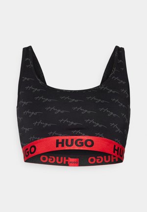 Black crop top bra with subtle gray "Hugo" text pattern, featuring a bold red elastic band with "HUGO" logo in black. Smooth fabric texture.