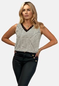 Biała tank top z czarnym wzorem kraty, z czarną koronką przy dekolcie. Połączona z czarnymi dopasowanymi spodniami i złotymi guzikami.