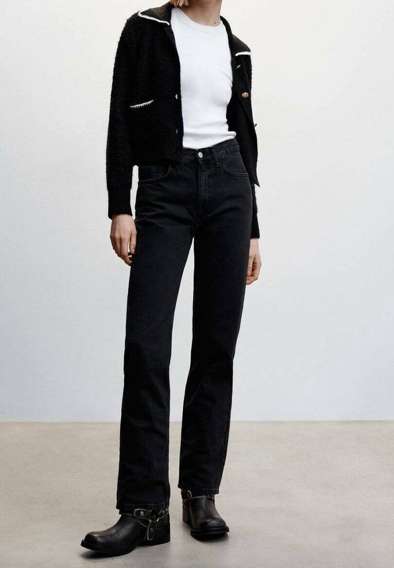 Cardigan noir texturé avec des bordures blanches contrastantes, porté sur une chemise blanche, associé à un jean noir taille haute et des bottines.