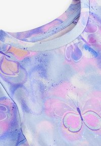 Hellblaues T-Shirt mit Rundhalsausschnitt, das einen Schmetterlingsdruck in rosa und lila Farbtönen vor einem weichen, strukturierten Hintergrund zeigt.