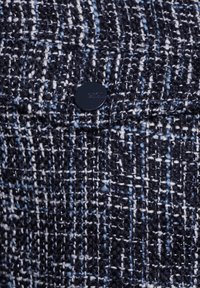 Tessuto tweed blu navy con una finitura testurizzata, dotato di un bottone circolare nero e un sottile motivo tessuto.