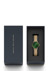 Gold mesh-Armbanduhr mit grünem Zifferblatt, präsentiert in einer dunkelblauen Box mit schwarzem Innenraum. Merkmale ein minimalistisches Design und dezente Stundenmarkierungen.