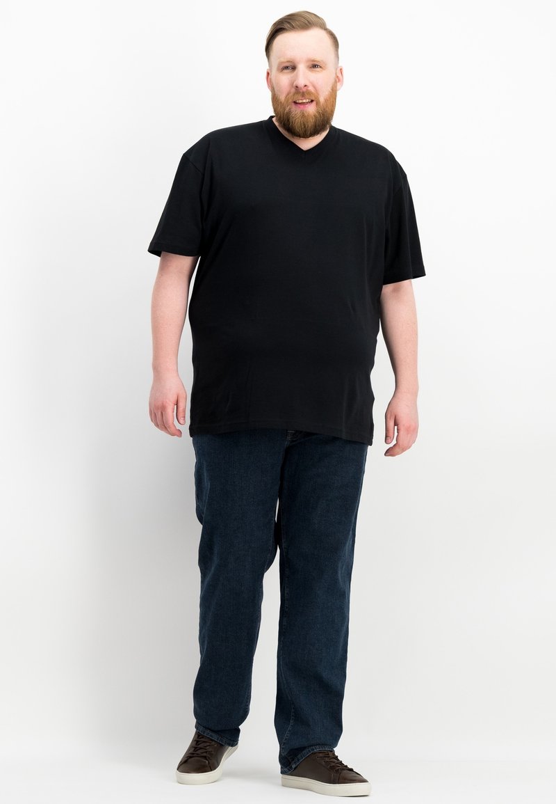 Schwarzes V-Ausschnitt-T-Shirt aus Baumwolle, kombiniert mit dunklen Jeans. Die Jeans haben einen geraden Schnitt und werden mit dunklen Sneakers getragen.