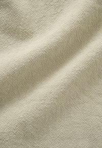 Tissu beige clair avec un motif tissé texturé montrant des plis doux et un drapé naturel et souple.