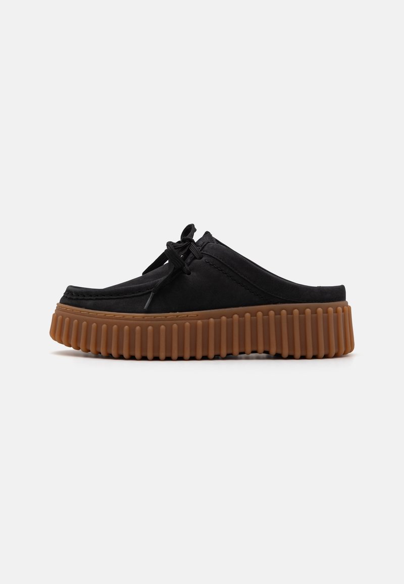 Chaussure noire à enfiler avec lacets et semelle épaisse en caoutchouc brun rainurée, présentée en profil sur fond blanc.