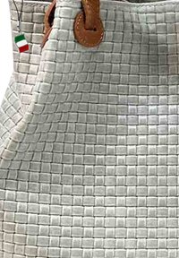 Sac en toile tissé de couleur gris clair avec une surface texturée, comportant des accents en cuir brun et un petit charm en forme de drapeau italien.