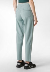 Pantalones de un verde claro, de corte relajado, con una cinturilla elástica, dos bolsillos traseros y una textura suave; combinados con zapatillas deportivas negras.
