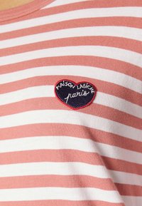 Gestreiftes T-Shirt in Koralle und Weiß, mit einem herzförmigen gestickten Aufnäher, auf dem "MAISON LABICHE" und "paris" in weißem Text auf navy Hintergrund zu sehen sind.