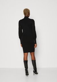 Sort tæt dress med høj hals, lange gennemsigtige ærmer med teksturerede mønstre, parret med knæhøje, glinsende sorte støvler.