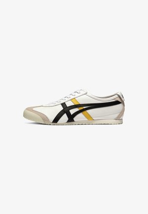 Sneaker bianca bassa con strisce nere e gialle, punta in camoscio beige, lacci bianchi e suola piatta.