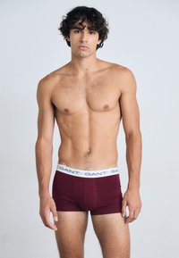 Boxers cortos burdeos con una cinturilla elástica blanca que presenta la marca "GANT". Tejido suave y diseño ajustado que proporciona un ajuste ceñido.