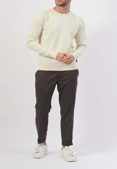 Maglione di lana leggermente beige con maniche lunghe e scollatura rotonda; abbinato a pantaloni scuri a sigaretta marrone scuro e sneakers bianche.