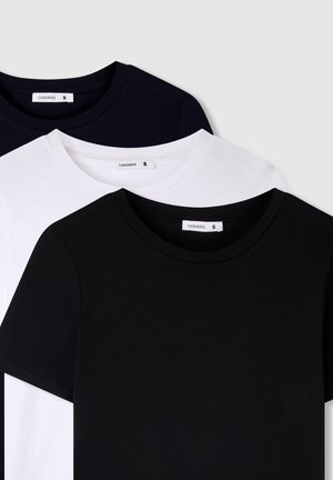Tre magliette semplici della marca Terranova in nero, bianco e blu scuro, impilate sovrapposte con le etichette del collo che mostrano la taglia S.