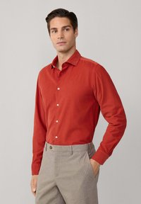 Rotes Langarmhemd mit Button-Down-Kragen, glatter Textur und weißen Knöpfen; kombiniert mit grau karierten Hosen.