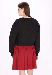 Sudadera negra recortada con mangas largas combinada con una falda plisada roja. Textura de tela suave, colores contrastantes y diseño sencillo.