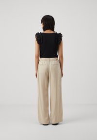 Svart topp med volangiga genomskinliga ärmar, matchad med ljusbeige vida byxor med elastisk midja och bakfickor.