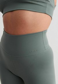 Grijze high-waisted legging gemaakt van gladde, rekbare stof. Voorzien van een logo op de tailleband en subtiele naaddetails.