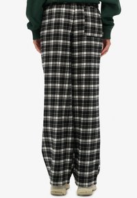 Czarno-białe spodnie w kratę o luźnym kroju, z elastycznym pasem i tylną kieszenią, wykonane z miękkiego materiału o gładkiej fakturze.