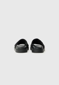 Sorte sandaler med en glatt lærfotseng og mykt stoffoverdel, med et åpent design og flate gummisåler.