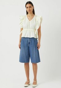 Witte, gerimpelde blousetop met een V-hals en een trekkoord in de taille, gecombineerd met blauwe denim culottes en crèmekleurige schoenen.