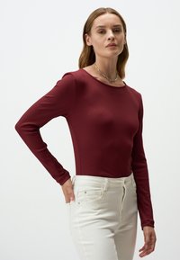 Bordeaux langemouwen top met een geribbelde textuur en ronde hals, gecombineerd met witte high-waisted jeans met een ritsluiting en zijzakken.