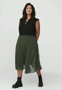 Fekete, ujjatlan felső, fodros szélekkel, olívazöld, redőzött szoknyával és fekete fűzős csizmával párosítva. Egyszerű dizájn és lágy anyag.