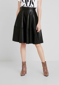 Falda midi de piel sintética negra con silueta acampanada, cuenta con dos costuras horizontales. Combinada con botas de tobillo de piel de serpiente rosas.