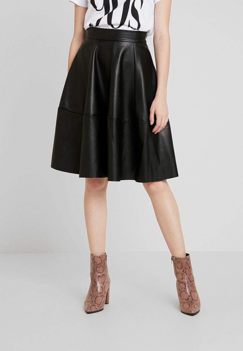 Falda midi de piel sintética negra con silueta acampanada, cuenta con dos costuras horizontales. Combinada con botas de tobillo de piel de serpiente rosas.