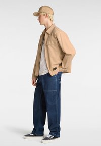 Beige button-up jacket with two chest pockets over a light shirt, paired with loose-fitting dark denim jeans and black/white sneakers.