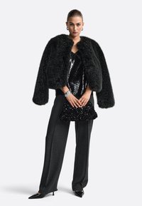 Čierna umelá kožušina skrátená bunda, korálkový top, strihané čierne nohavice a trblietavá kabelka. Doplnky zahŕňajú strieborné náramky.