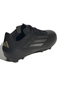 Scarpa da calcio nera con tomaia sintetica texturizzata, chiusura con lacci e logo a tre strisce rialzato sul lato. Presenta tacchetti modellati per la presa.