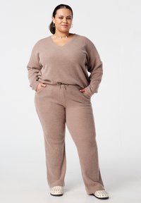 Beige gebreide lounge set met een V-hals trui met lange mouwen en broeken met elastische tailleband, beide met een gestructureerde weefsel. Verstelbare koord.