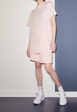 Lichtroze T-shirt met korte mouwen, gecombineerd met bijpassende shorts. Witte sneakers met opvallende veters en gestructureerde zolen.